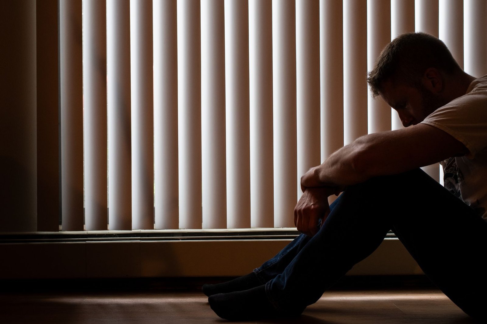Depression Awareness Certification - A man sits silhouetted against window blinds, conveying solitude and introspection.