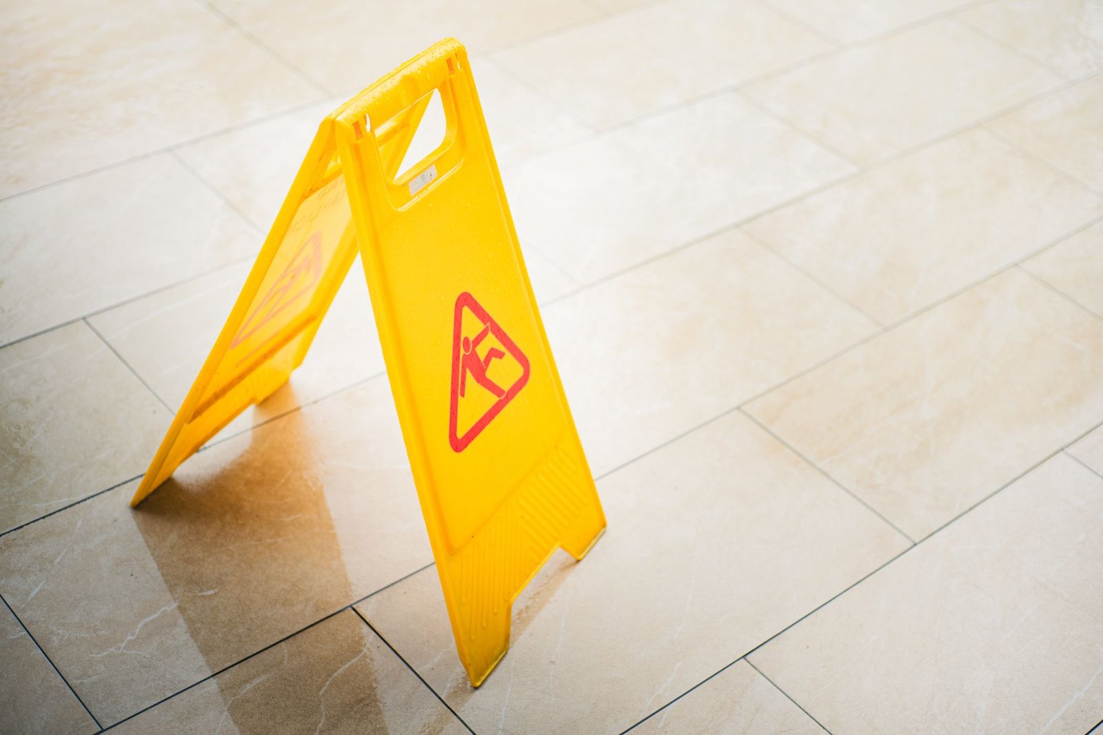Product Liability Certification - A bright yellow caution sign on a tiled floor indicates a wet surface, alerting passersby to potential hazards.