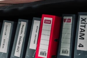 Developing and Implementing New Admin Systems Certification - Color-coded office binders organized neatly in a storage shelf, featuring labels and a striking red binder.