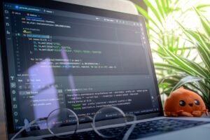 Software Testing Certification - Open laptop displaying code next to a plush toy, set in a bright room with plants.