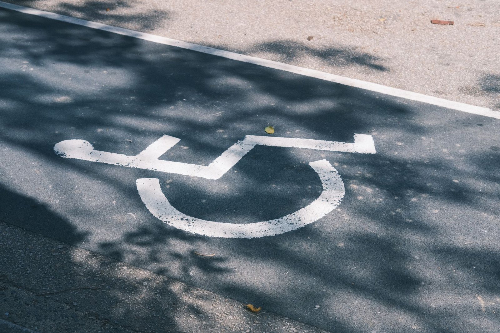 Disability Awareness Certification - Close-up of an accessible parking symbol on a sunlit asphalt road.