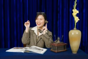 Learning Impressive Telephone Techniques Certification - Woman in retro attire smiling while using a vintage phone, with a decorative vase on a table.