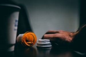 Drug and Alcohol Awareness Certification - Moodily lit scene of an open prescription bottle and hand on a table, depicting healthcare themes.