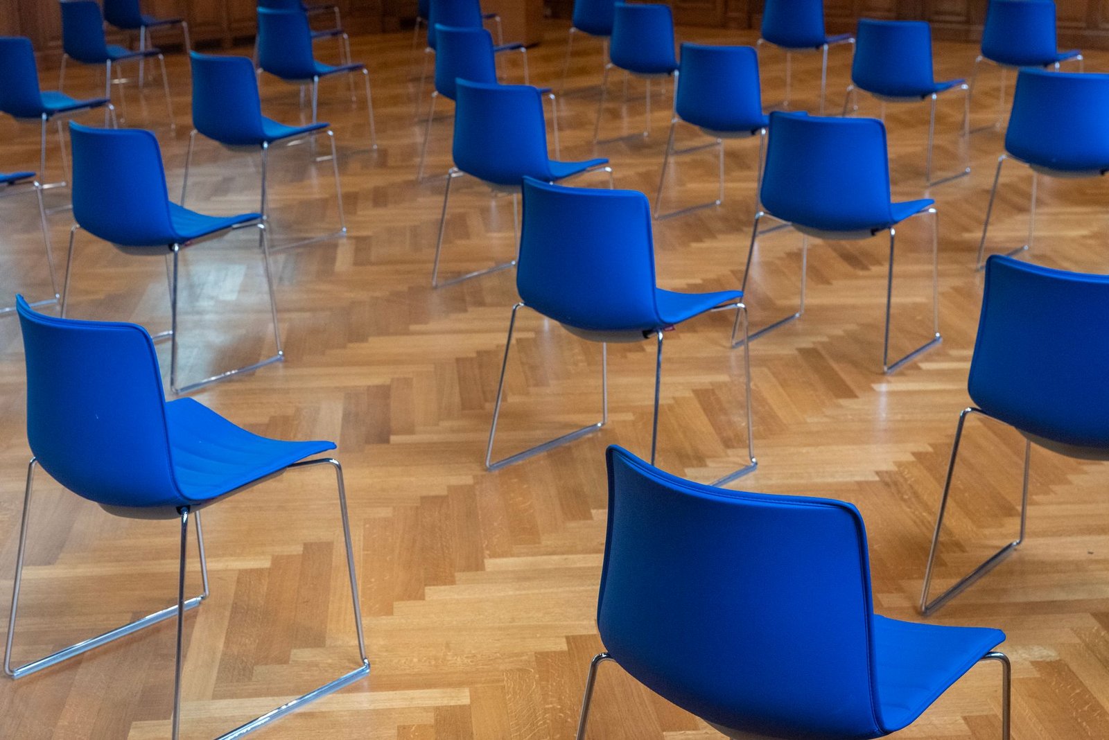 Organising and Chairing Meetings Certification - Empty room with blue chairs on a wooden parquet floor, arranged in rows.