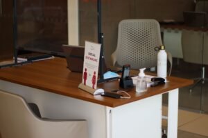 Office and Reception Management Certification - Office desk featuring laptop, sanitizer, and social distancing sign during the day.