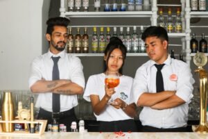 Bartending Certification - Three bartenders in a bar setting, discussing cocktails, surrounded by liquor bottles.