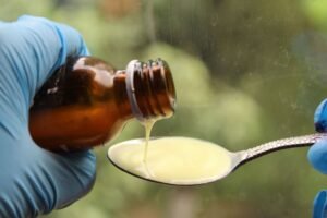 Fluids and Nutrition in Care Certification - Close-up of liquid medicine being poured into a spoon, captured with gloves for medical use.
