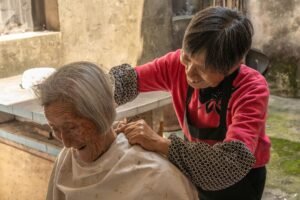 Caring for the Elderly Certification - An elderly woman receives a haircut from another woman in a rustic outdoor setting.