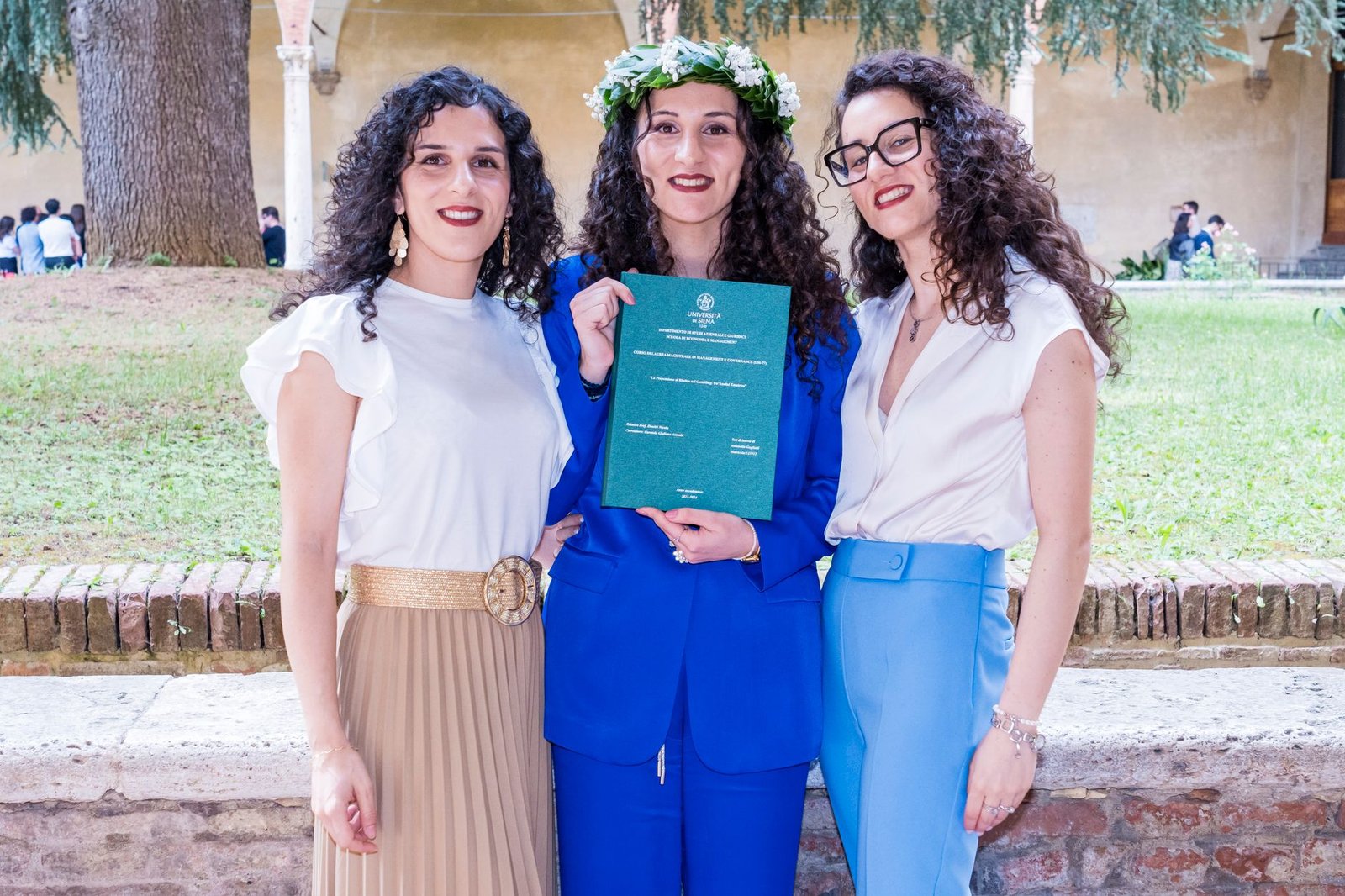 Fashion Design Diploma - Three women posing together outdoors, one holding a graduation diploma.