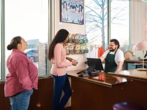 Managing and Improving Customer Service Process Certification - Two customers interacting with staff at a restaurant point of sale counter.