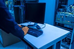 Computer Maintenance Certification - An IT professional operates a computer in a server room, managing network systems and connected devices.