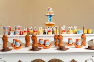 Cupcake Decorating – Birthday Ideas Pack 1 - Colorful toy-themed birthday party table with decorations, cupcakes, and creative cowboy boot cups.