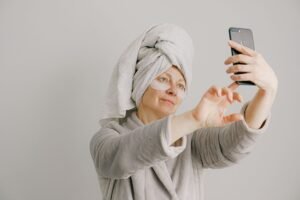 Selfie Masterclass: How to Take Perfect Selfies Certification - Woman in a bathrobe with skincare pads taking a selfie, promoting self-care and relaxation.