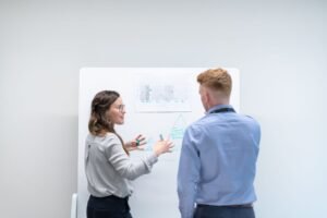 Delivering Useful Feedback in a Corporate Setting Certification - Two professionals discussing project plans at whiteboard in office setting.