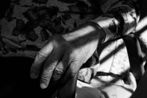 Privacy and Dignity Certification - Black and white photo of an elderly hand resting on a chair, showing age and texture.