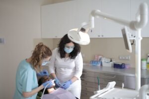Dental Assistant Certification - Young female dentist in medical mask and latex gloves curing teeth of patient with assistant using medical instruments in modern dental clinic