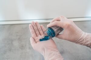Safe Handling of Medicines Foundation Certification - Close-up of gloved hands pouring blue pills from a bottle, illustrating medication and healthcare.