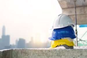 Head Protection Awareness Certification - Three colorful safety helmets stacked on a concrete surface with city skyline in background.