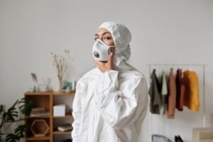 Personal Safety Certification - A woman in a PPE suit and mask stands indoors with clothes and plants around.