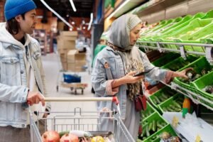Consumer Rights Awareness Certification - Diverse couple shopping for vegetables in a supermarket, discussing choices with smartphone.
