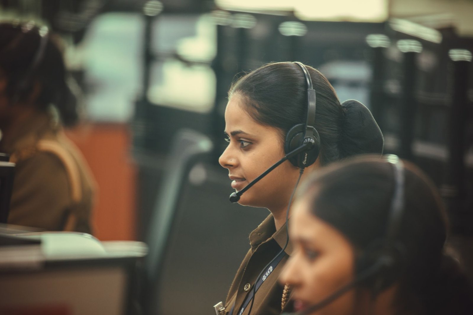 Telephone Customer Services Certification - Side view of a call center agent wearing a headset, working diligently in a busy office environment.
