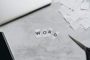Microsoft Word Certificate Level 1 - Top view of a workspace with scattered paper letters spelling 'WORD', next to a laptop and scissors.