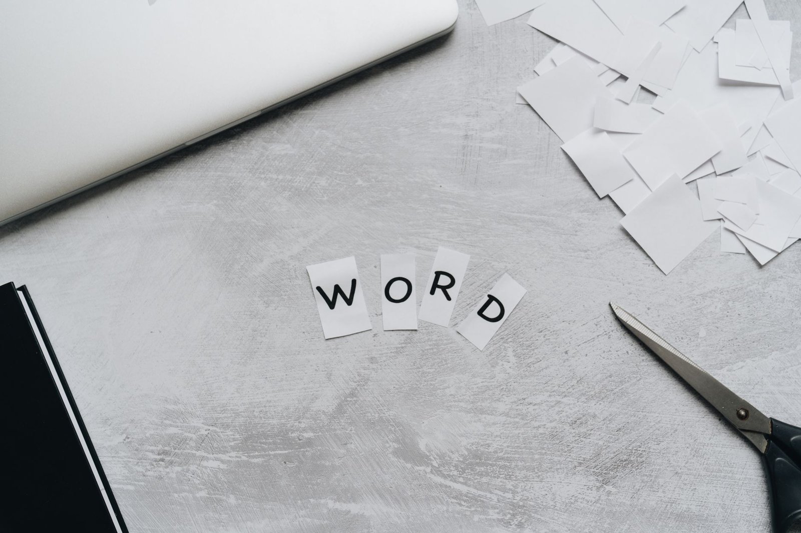 Microsoft Word Certificate Level 1 - Top view of a workspace with scattered paper letters spelling 'WORD', next to a laptop and scissors.