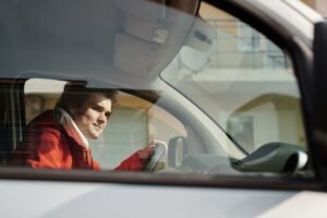 Introduction to Driver Safety Certification - A man in a red jacket driving a car, seen through the window on a sunny day.