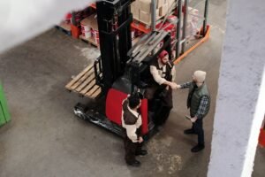 Manual Handling Interactive Certification - Three warehouse workers in conversation and handshake next to a forklift in an industrial setting.