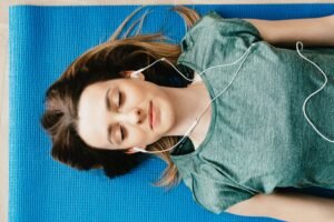 Reducing Stress with Meditation and Visualisation Certification - From above of calm young female in casual wear listening to music in earphones while taking break after workout on blue mat in flat