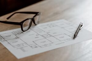 Project Preparation Certification - From above of eyeglasses near pen on plan placed on wooden table in apartment in soft daylight