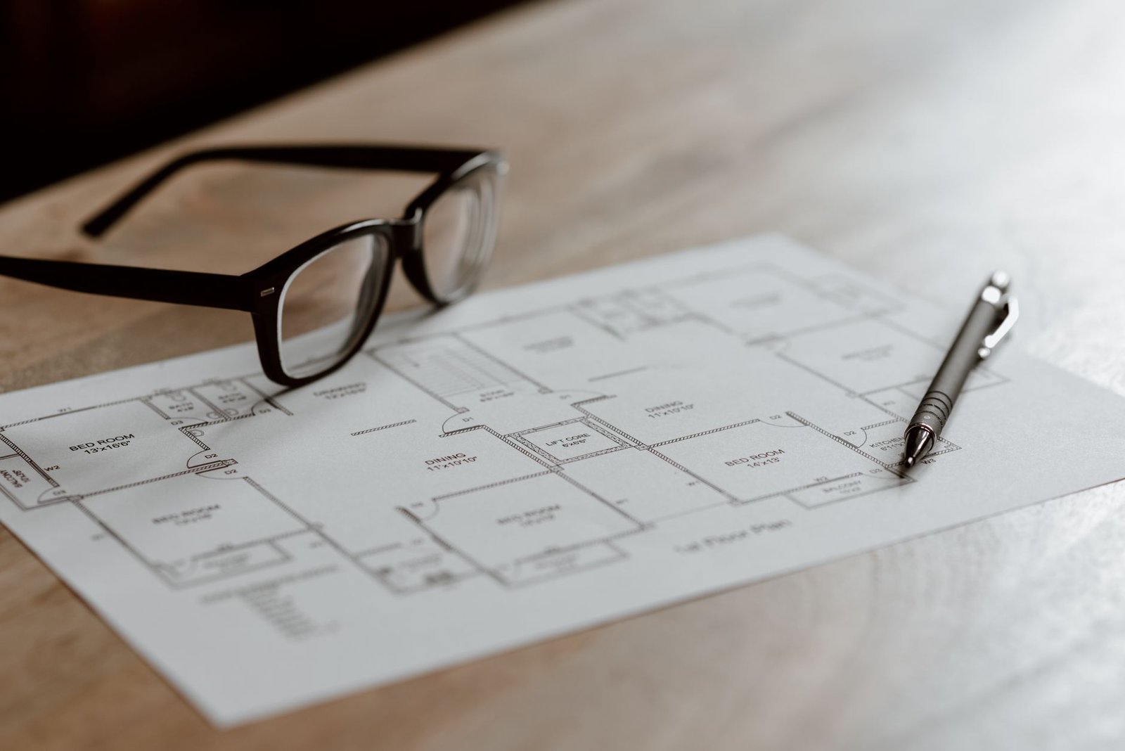 Project Preparation Certification - From above of eyeglasses near pen on plan placed on wooden table in apartment in soft daylight