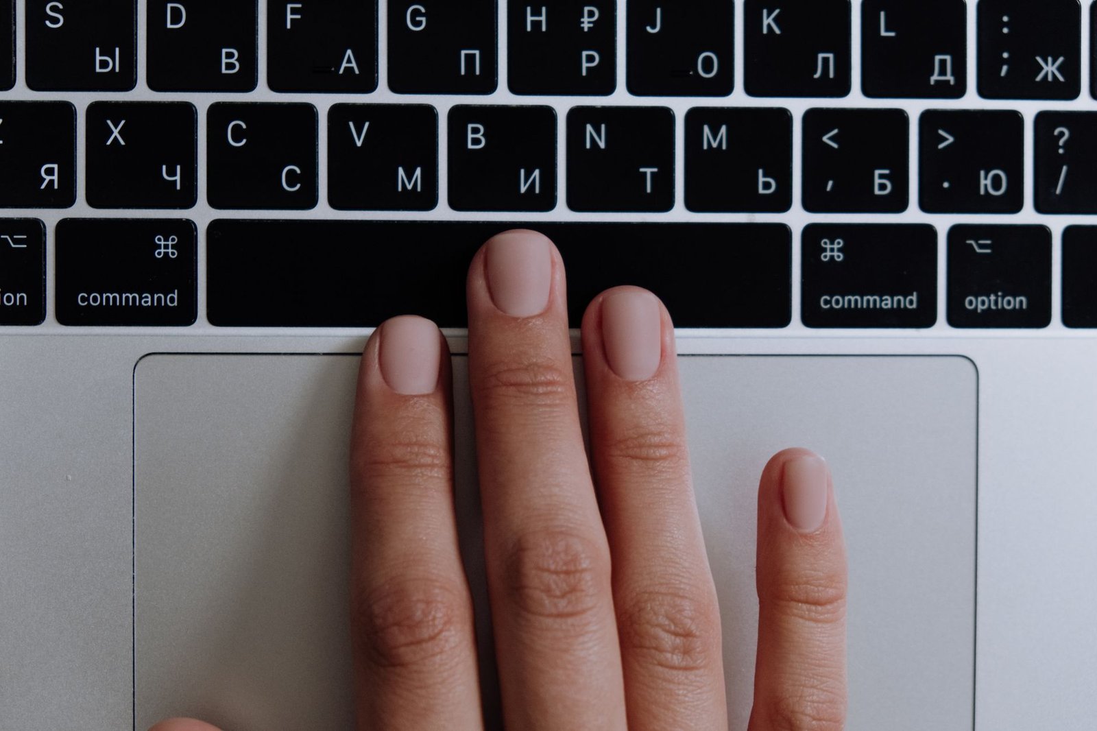 Touch Typing and Shorthand Certification - A close-up of a hand typing on a silver laptop with a Russian keyboard layout, showcasing modern technology.