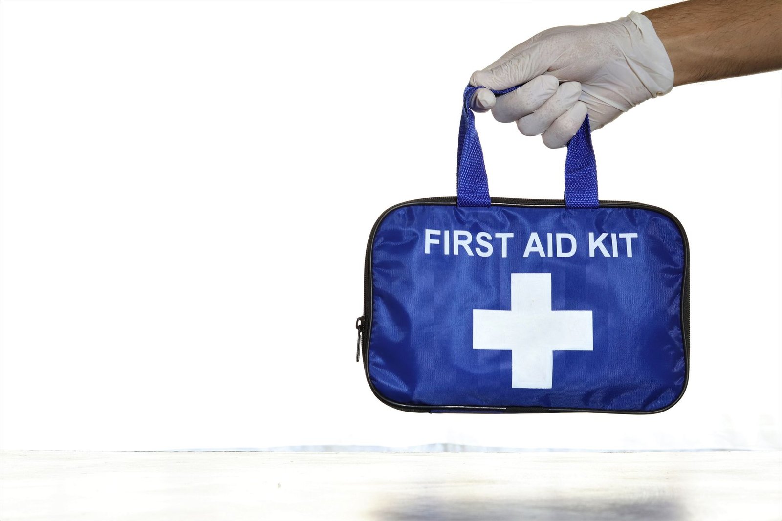 Pet First Aid Certification - Close-up of a blue first aid kit held by a hand in a latex glove against an isolated white background.