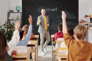 Managing Classroom Behaviour Certification - Teacher interacting with students raising hands in a classroom setting.