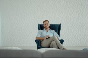 Master Hypnotherapist Certificate - A thoughtful man sitting cross-legged in an armchair against a stylish white background.