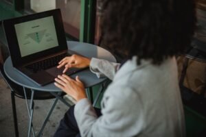 Sales Funnels for Beginners Certification - Back view of anonymous ethnic female in suit working with chart on computer while sitting at table in outdoor cafe during remote work