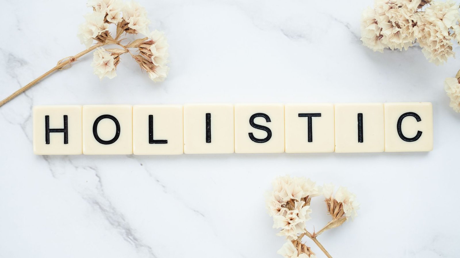 Introduction to Holistic Health Certification - Flat lay of 'holistic' spelled in letter tiles on marble with dried flowers.