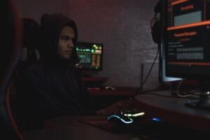 Insider Threat - A hacker in a hoodie working in a dimly lit room, focusing on cyber security tasks on multiple monitors.