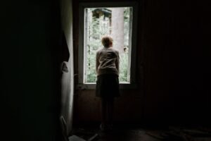 Child Sexual Exploitation Awareness Certification - A young child curiously looks through a window of an abandoned building into the greenery outside.