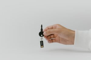 MFA and Passkeys - Hand holding keychain with integrated USB flash drive against a plain background.