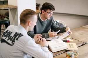 Basic English Certification - Two young men studying together, focusing on English grammar books in a modern indoor setting.