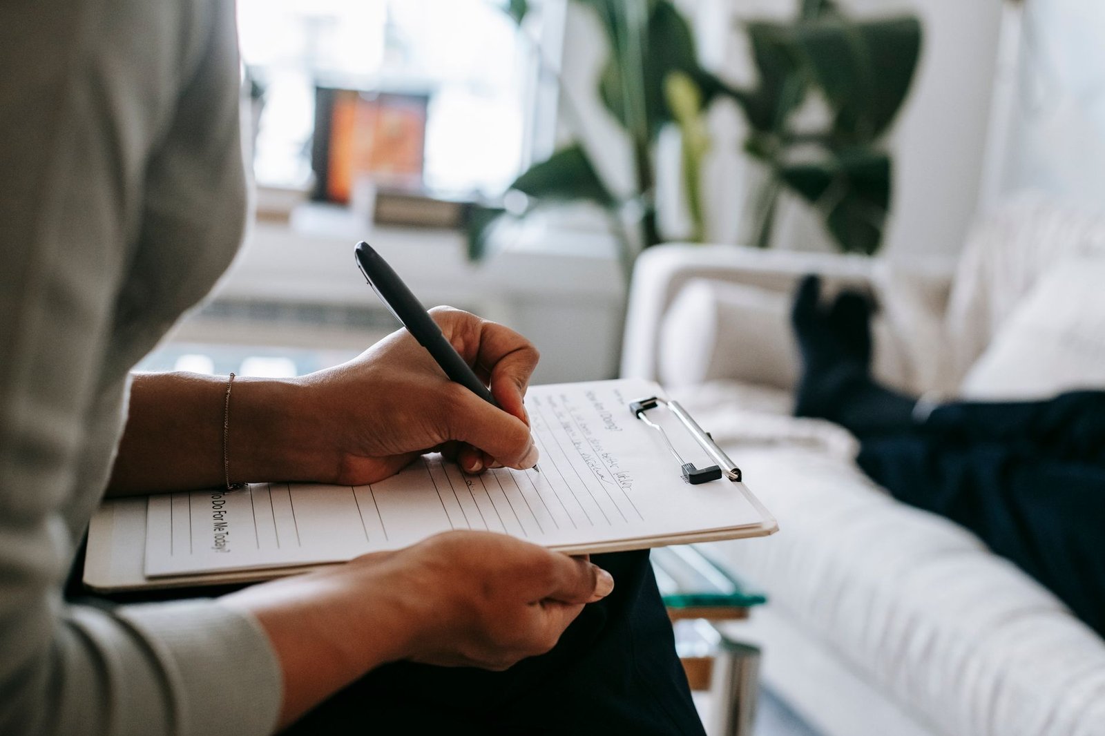 Professional Psychotherapy Certificate - Unrecognizable ethnic female therapist taking notes on clipboard while filling out form during psychological appointment with anonymous client lying on blurred background