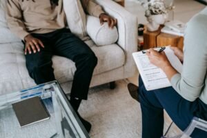 Professional Post-Traumatic Stress Disorder Counselling Certification - From above crop African American male in casual clothes sitting on comfy couch and answering professional female consultant questions in modern psychotherapy office