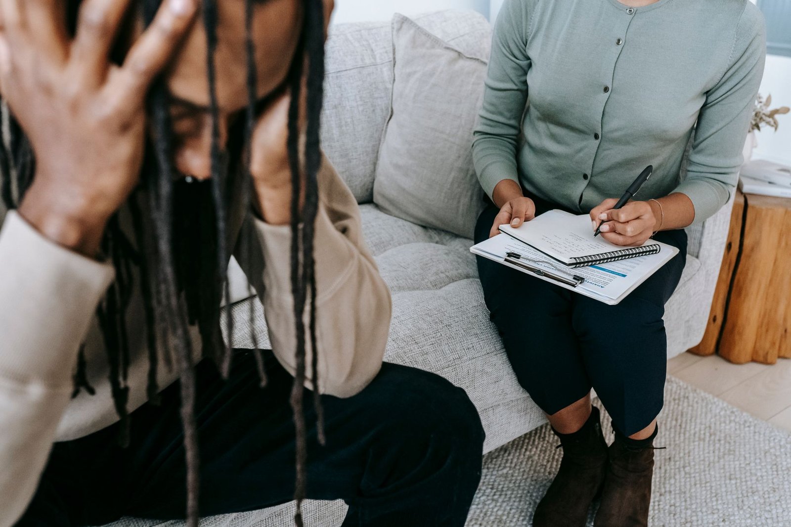 Counselling Certification - Crop concerned African American male sitting on sofa with female psychologist and holding head in hands in dismay during psychotherapy session
