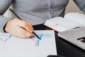 Business Report Writing Certification - A business analyst examines a graph on paper with a laptop and notebook indoors.