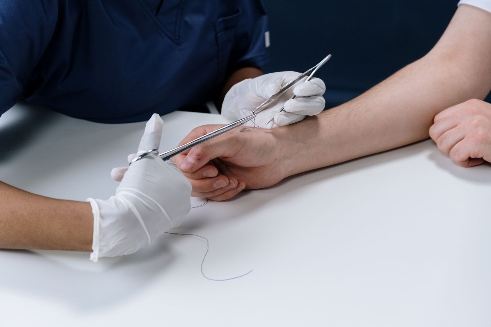 Sharps Injuries Awareness Certification - Medical professional suturing an injury on a person's arm with surgical instruments.