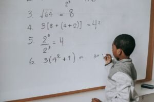 Introduction to Maths Certification - Side view of concentrated African American pupil standing near whiteboard in classroom and solving math examples during lesson at school