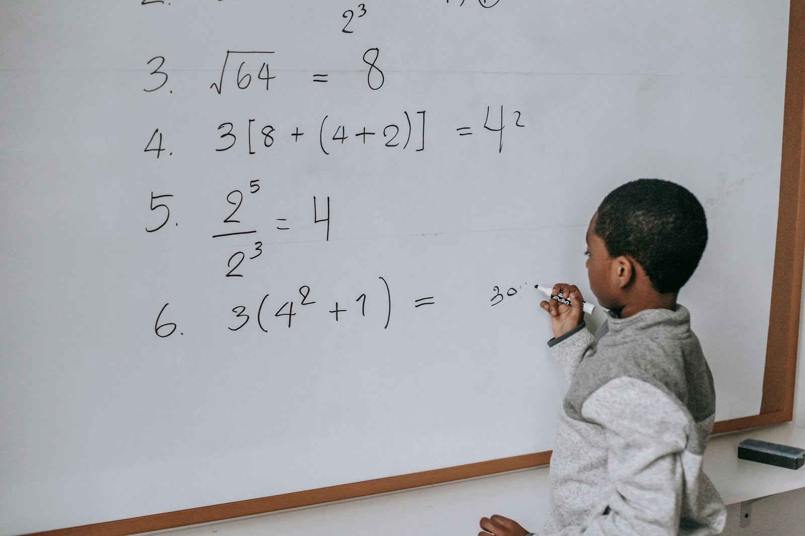 Introduction to Maths Certification - Side view of concentrated African American pupil standing near whiteboard in classroom and solving math examples during lesson at school