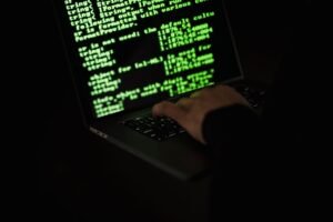 Understanding Malware - Crop unrecognizable computer geek typing on netbook with codes on screen while hacking system in darkness
